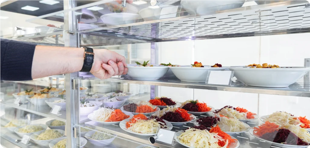 A man's hand taking fresh food from a stocked shelf.