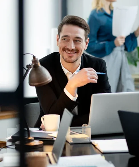 A man in an office, smiling while looking at something.
