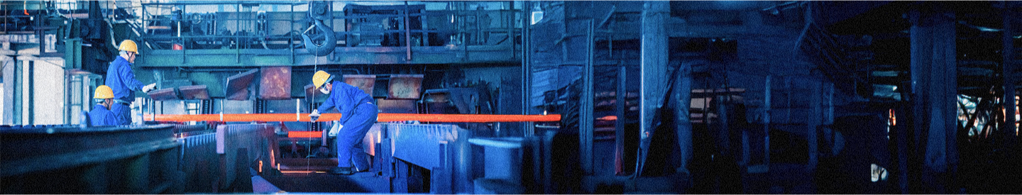 Three manufacturers wearing blue onesies and yellow caps inside a factory.