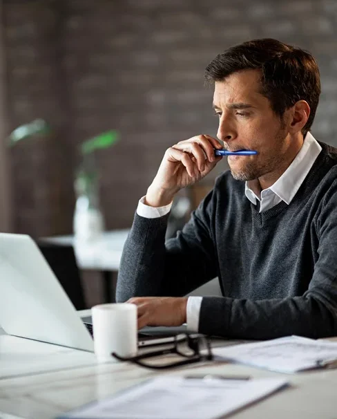 A man engrossed in work, holding a pen between his lips.