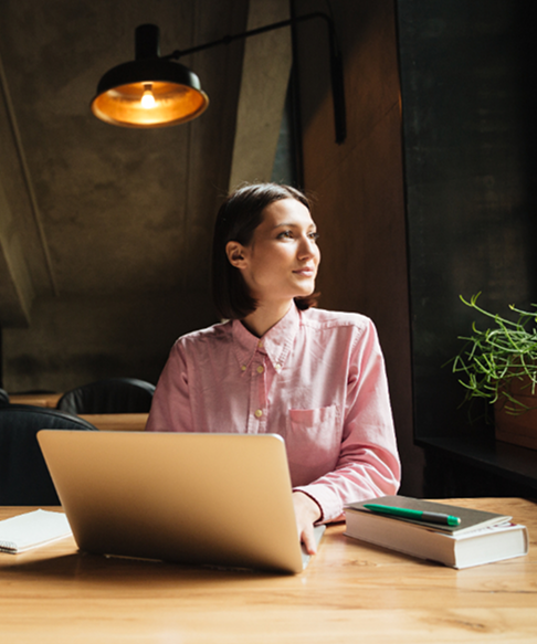 A woman smiling sideways with a laptop in front of her and a warm yellow light in the background.